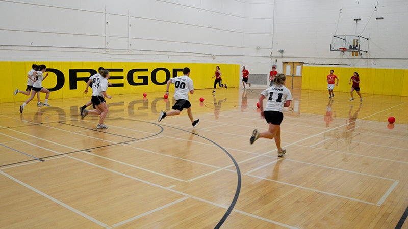 Students in a gymnasium, racing to pick up balls on the center line