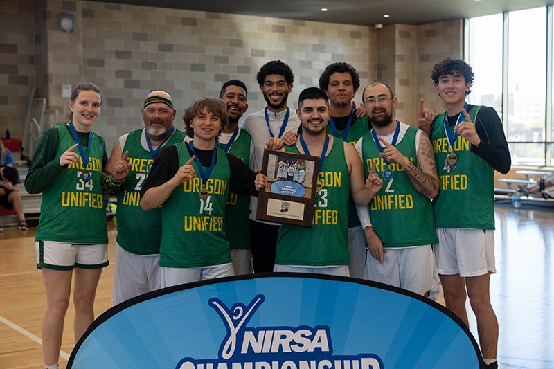 Nine people pose for a photo holding their basketball championship trophy