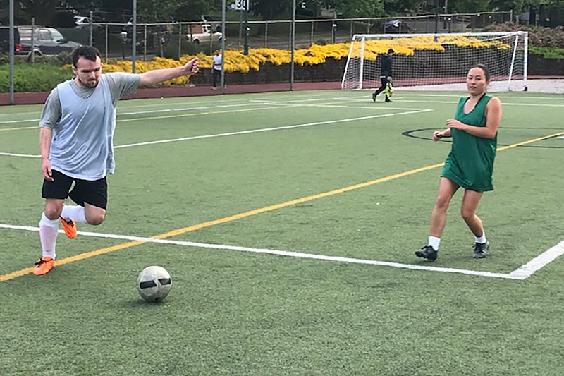 Two people play soccer on a turf field