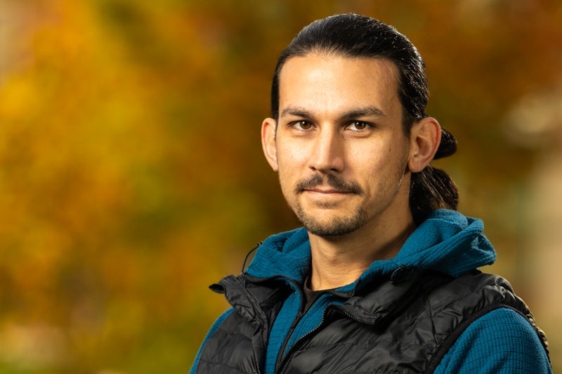 man with black hair and mustache and beard wearing a black puffy vest