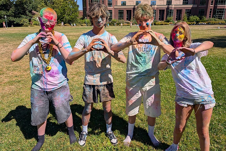 Four teenagers covered in colors form their hands into letter O