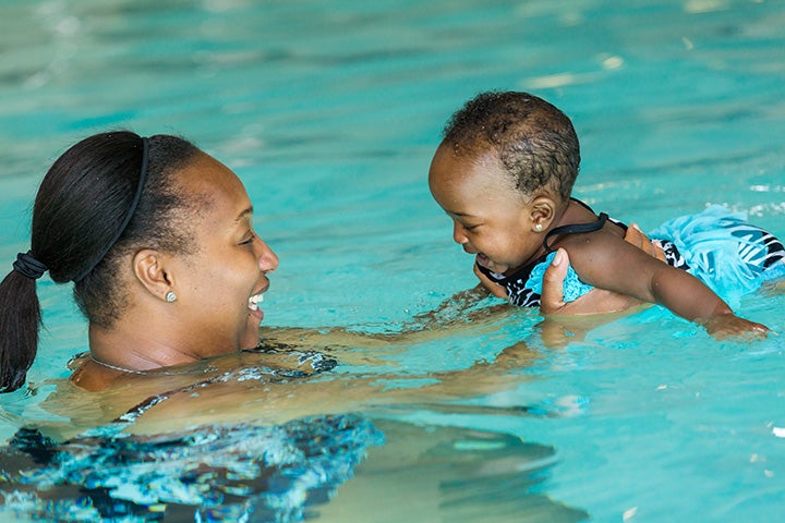 A mom hold her baby up in the pool during a swim lesson.